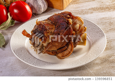 Roasted pork knuckle with crispy skin served on a plate with fresh tomatoes and garlic on a wooden table Roasted pork knuckle with crispy skin served on a plate with fresh tomatoes and garlic on a wooden table 139396851