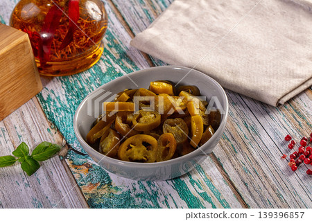 Sliced pickled jalapeno peppers in a bowl on a rustic table with spices and herbs 139396857