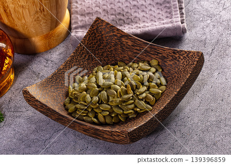 Raw green pumpkin seeds in a rustic wooden bowl on a textured grey background Raw green pumpkin seeds in a rustic wooden bowl on a textured grey background 139396859