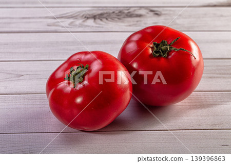 Close up of two organic red tomatoes with green stems on a rustic wood surface Close up of two organic red tomatoes with green stems on a rustic wood surface 139396863