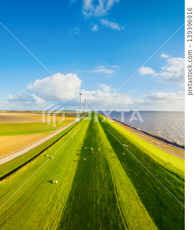Aerial view of wind turbines on green fields near sea coast and dam.  139396916