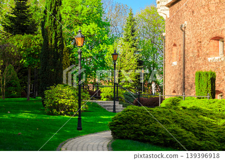 Idyllic park pathway with historic brick building and lush green landscaping Idyllic park pathway with historic brick building and lush green landscaping 139396918