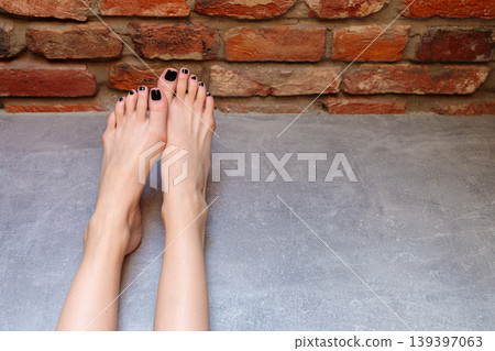 Woman bare legs with black toenails on gray floor against brick wall background 139397063