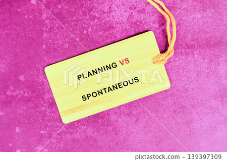 A yellow wooden tag with an orange string contrasts planning and spontaneous approaches. The message is displayed against a vibrant fuchsia textured surface, highlighting choice A yellow wooden tag with an orange string contrasts planning and spontaneous approaches. The message is displayed against a vibrant fuchsia textured surface, highlighting choice 139397309