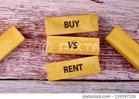 Three wooden blocks clearly display the words BUY, VS, and RENT, arranged on a distressed wooden surface with peeling white and red paint Three wooden blocks clearly display the words BUY, VS, and RENT, arranged on a distressed wooden surface with peeling white and red paint 139397326