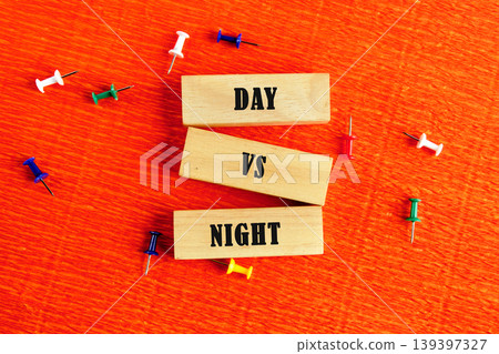 Three wooden blocks are stacked vertically on a vibrant orange textured surface. They spell Day vs Night, illustrating a time comparison Three wooden blocks are stacked vertically on a vibrant orange textured surface. They spell Day vs Night, illustrating a time comparison 139397327