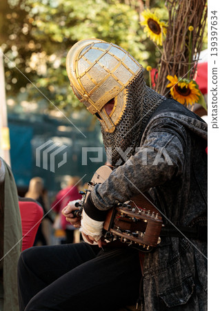 Medieval knight character in ornate helmet plays a hurdy gurdy at an outdoor festival 139397634