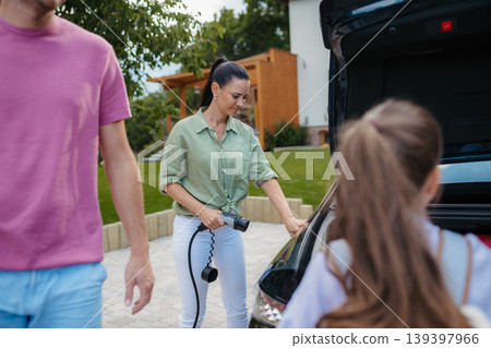 Mother charging electric car while family prepares for summer trip. Mother charging electric car while family prepares for summer trip. 139397966