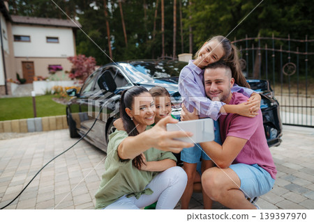 Happy family taking selfie in front of their charging electric car. Happy family taking selfie in front of their charging electric car. 139397970
