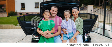 Happy family sitting in car trunk and waiting for electric car charging. Happy family sitting in car trunk and waiting for electric car charging. 139397971