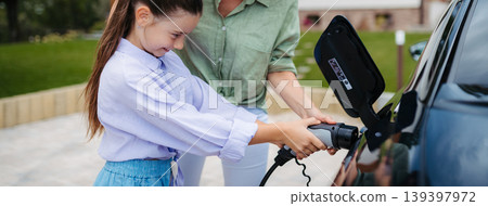 Mother and girl charging electric car while family prepares for summer trip. 139397972