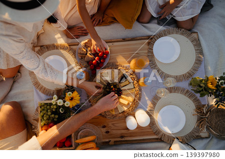 Top view of picknic blanket and hands picking food from plates. 139397980