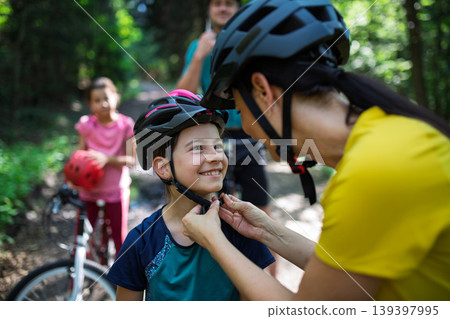 Mother fastening helmet on daughter before cycling for safety. 139397995
