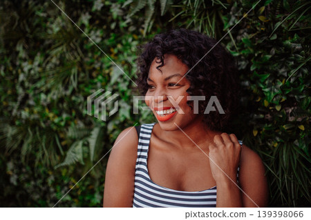 A portrait of a black woman standing against green background of bush leaves. A portrait of a black woman standing against green background of bush leaves. 139398066