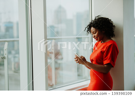 Beautiful african-american woman standing by the window checking her phone. Beautiful african-american woman standing by the window checking her phone. 139398109