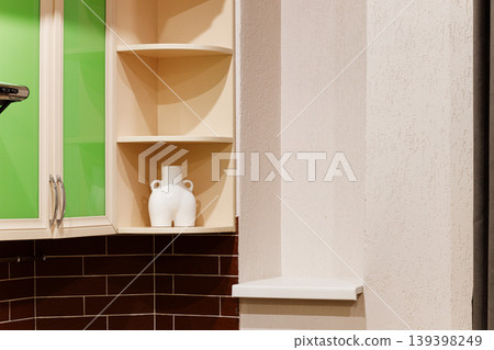 A white vase sits on a shelf in a kitchen with brown tiles and green cabinet doors A white vase sits on a shelf in a kitchen with brown tiles and green cabinet doors 139398249