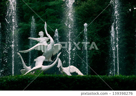 Ornate fountain sculpture featuring a child riding swans amidst cascading water jets in a lush park Ornate fountain sculpture featuring a child riding swans amidst cascading water jets in a lush park 139398276
