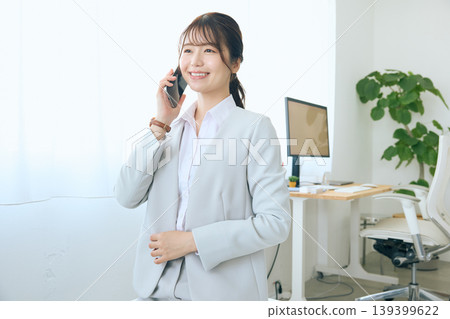 A young businesswoman talking on her smartphone; an office worker answering the phone in the office. A young businesswoman talking on her smartphone; an office worker answering the phone in the office. 139399622