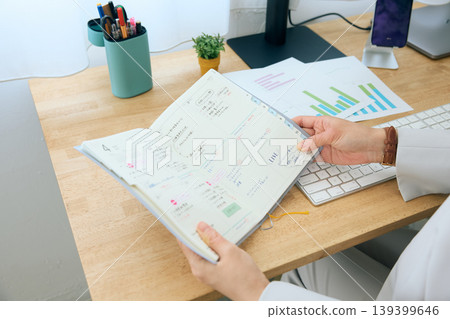 A typical office scene: a female business person checking her schedule book at her desk. 139399646