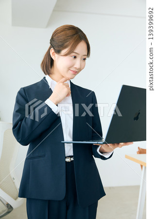 A young female business person in the office, holding her laptop and making a triumphant gesture; a group of motivated people in suits. A young female business person in the office, holding her laptop and making a triumphant gesture; a group of motivated people in suits. 139399692