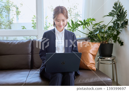 Image of a young female business person working remotely or from home, sitting on a sofa and using a laptop. 139399697