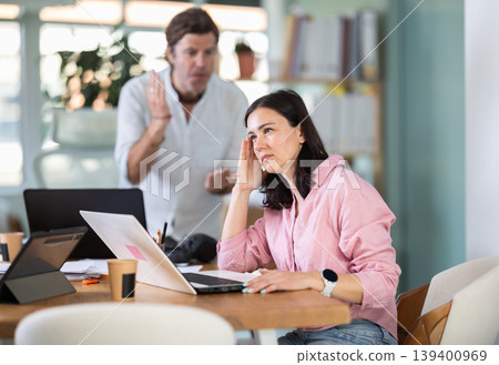Adult man scolding adult female colleague working on laptop 139400969