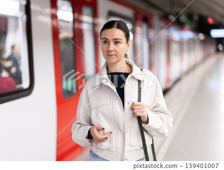 Girl is standing on metro platform station, waiting for transport to arrive 139401007