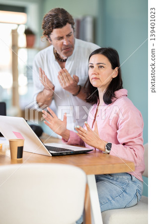 Adult man scolding adult female colleague working on laptop 139401023
