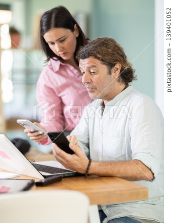 Middle-aged male and female colleagues looking at smartphone at office Middle-aged male and female colleagues looking at smartphone at office 139401052