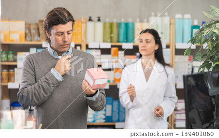 Middle-aged man choosing pills in box while pharmacist offering in drugstore Middle-aged man choosing pills in box while pharmacist offering in drugstore 139401060