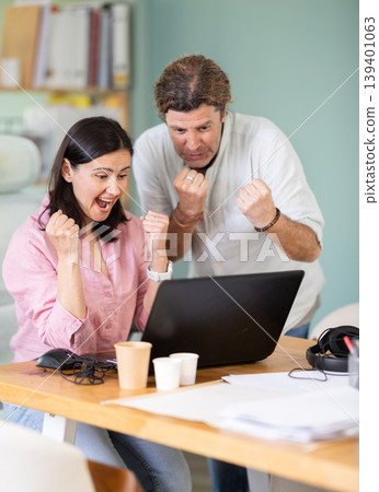 Happy colleagues sharing success while looking at laptop screen Happy colleagues sharing success while looking at laptop screen 139401063