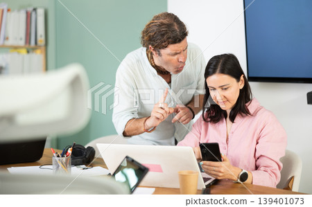Businessman complains to subordinate about her talking on her mobile phone while working in office 139401073