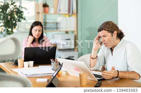 Sad and puzzled man working on laptop with problems in office Sad and puzzled man working on laptop with problems in office 139401083