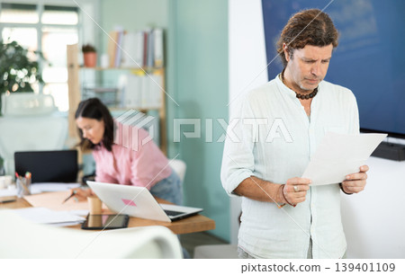 Middle-aged man reviewing documents while standing in office 139401109