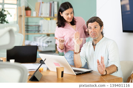 Adult woman scolding adult male colleague working on laptop 139401116