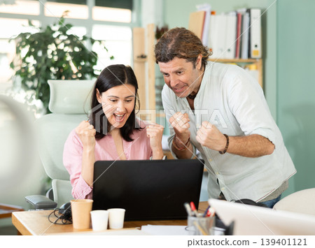 Happy colleagues sharing success while looking at laptop screen Happy colleagues sharing success while looking at laptop screen 139401121