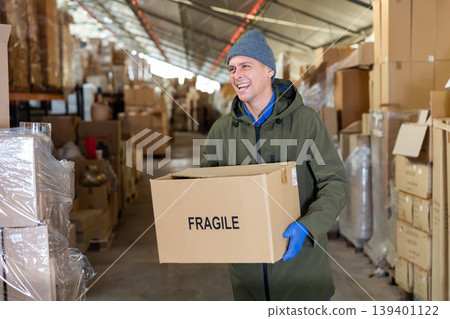 Positive worker carrying cardboard box with fragile content 139401122