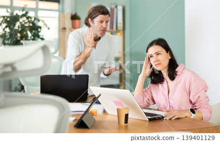 Adult man scolding adult female colleague working on laptop 139401129