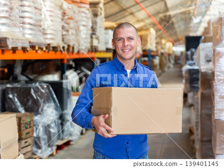 Positive warehouse worker dragging boxes on hands 139401145