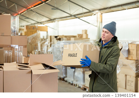 Warehouse worker carrying boxes on racks in in warehouse 139401154