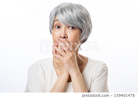 A senior woman with her hands covering her mouth and wide-eyed, looking surprised. A senior woman with her hands covering her mouth and wide-eyed, looking surprised. 139401478