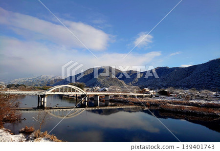 The snow-covered mountains and arch bridge are reflected on the calm surface of the river; a clear winter landscape. The snow-covered mountains and arch bridge are reflected on the calm surface of the river; a clear winter landscape. 139401743