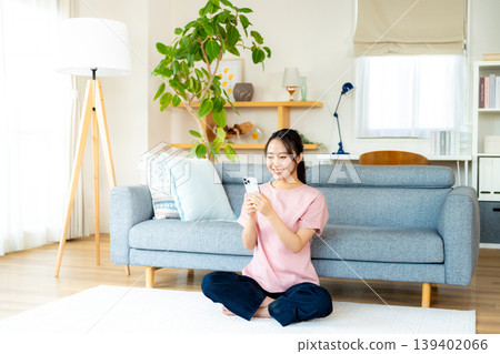 在房間裡操作智慧型手機的年輕女子 在房間裡操作智慧型手機的年輕女子 139402066