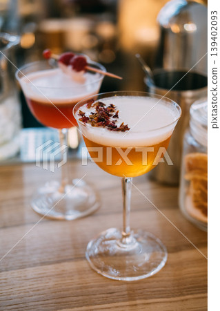 Garnished cocktail. Refreshing liquor mix. Stemmed glass with frothy liquid on tray. Restaurant alcohol with dried petals on wooden table. 139402093