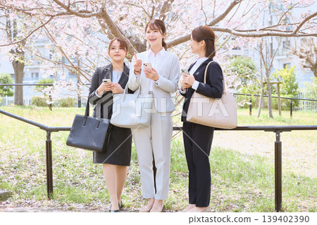 Three young businesswomen talking on their smartphones under the cherry blossoms – office ladies during the spring cherry blossom viewing season. Three young businesswomen talking on their smartphones under the cherry blossoms – office ladies during the spring cherry blossom viewing season. 139402390