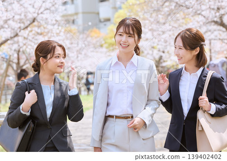 Three young female new employees walking under a row of cherry trees, smiling and chatting in suits—an image of a spring induction ceremony. Three young female new employees walking under a row of cherry trees, smiling and chatting in suits—an image of a spring induction ceremony. 139402402