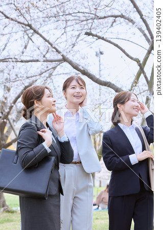 Three young women, new employees, walking under a row of cherry trees; businesswomen in spring recruitment suits. 139402405