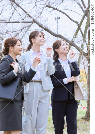 三位年輕的女性,新員工,走在一排櫻花樹下;春意盎然的新生景象;身著招募套裝的職業婦女。 三位年輕的女性,新員工,走在一排櫻花樹下;春意盎然的新生景象;身著招募套裝的職業婦女。 139402407