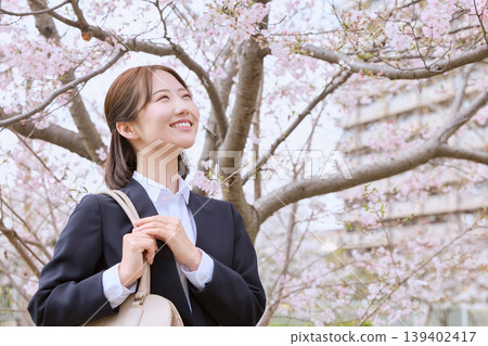 A young woman in a business suit smiles under the cherry blossoms – an image of springtime new beginnings and job hunting. A young woman in a business suit smiles under the cherry blossoms – an image of springtime new beginnings and job hunting. 139402417