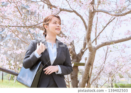 A young woman in a business suit, a new employee, walking under cherry blossoms – an image of spring job hunting. 139402503